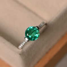 This ring features a 7mm round cut lab emerald and sterling silver finished with rhodium. Customization is available. It is made by hand, and it will take about 7 days to finish the ring after your payment is completed. Main stone: lab emerald Main stone weight: Approx 1.10 ct Metal type: sterling silver finished with rhodium Accent stone: cz Customization is available, I also can make it with 14k solid gold (white or yellow or rose) and diamond accent stone, just feel free to contact me. Any qu Emerald Ring With Center Stone In 14k White Gold, Classic Emerald Solitaire Rings, Classic Emerald Ring With Prong Setting For Promise, Classic Emerald Promise Ring With Prong Setting, Classic Emerald Ring With Prong Setting As Promise Ring, Emerald Solitaire Diamond Ring With Round Band, Formal Emerald Solitaire Birthstone Ring, Emerald Ring In White Gold With Brilliant Cut, Classic Emerald Ring With Round Stone