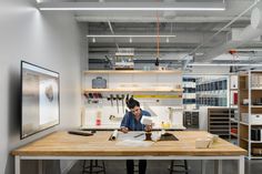 a man sitting at a desk in an office with lots of shelves and other items