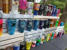 many different colored tumblers are lined up on a table with trees in the background