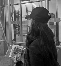 a woman with long dark hair is holding a book in her hand and looking out the window