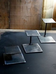 three metal square tables sitting on top of a black floor next to a wooden wall