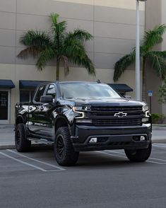 a black truck parked in front of a building with palm trees on the side of it