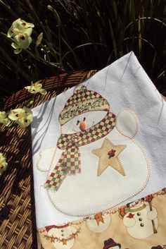 a white towel with a snowman on it sitting next to some flowers and grass