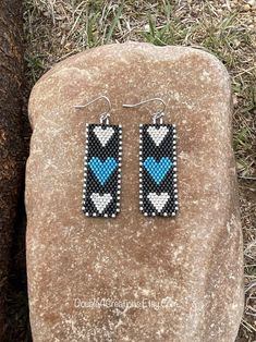 a pair of blue and black beaded earrings sitting on top of a rock