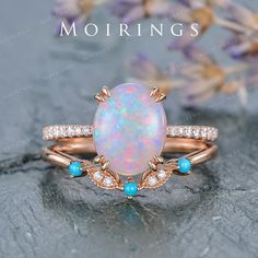 an opal and diamond ring set on top of a rock with flowers in the background