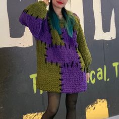 a woman with green hair wearing a purple sweater and black tights standing in front of a sign