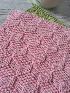 two crocheted blankets sitting on top of a wooden table next to a bowl