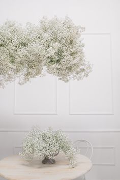 a white table topped with a vase filled with baby's breath next to a wall