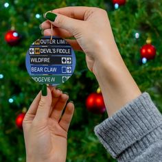 someone holding up a christmas ornament in front of a tree