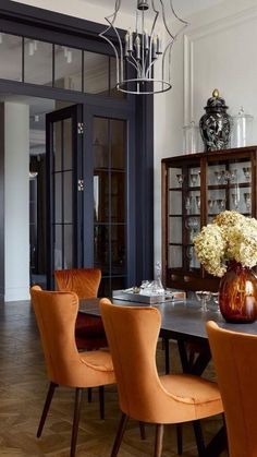 a dining room table with orange chairs and vases on top of it, in front of an open glass door