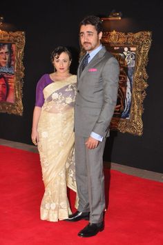 a man and woman standing on a red carpet in front of a wall with pictures