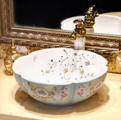 a fancy bowl sink in front of a mirror with gold trimmings and flowers on it