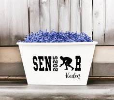 a white container filled with blue flowers next to a wooden fence