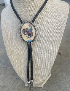 This awesome bolo tie has a vintage cowboy print with a clear resin coating and metal backing. Handmade in our shop! The cord is black and genuine leather. Our bolos pair nicely with many of our belt buckles! They make wonderful gifts.    The western bolo tie rope length is 39' ;  pendant size is 1 1/2'' x 1 1/4'' Cowboy Jewelry Men, Bolo Tie Tattoo, Vintage Adjustable Hand Tooled Bolo Tie, Adjustable Vintage Hand Tooled Bolo Tie, Vintage Bolo Tie With Adjustable Length For Western Events, Vintage Bolo Ties With Adjustable Length For Western-themed Events, Vintage Adjustable Jewelry For Western-themed Events, Adjustable Vintage Bolo Ties For Ranch, Vintage Brown Jewelry For Rodeo