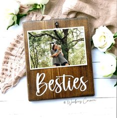 a wooden photo frame with the words besties on it and white flowers around it