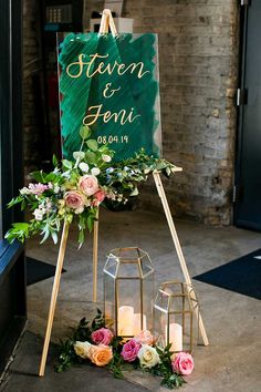 an easel with flowers and greenery on it is next to a candle holder