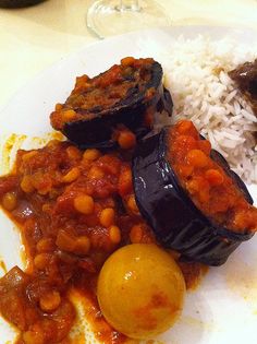 a white plate topped with meat and beans covered in sauce next to rice on top of a table