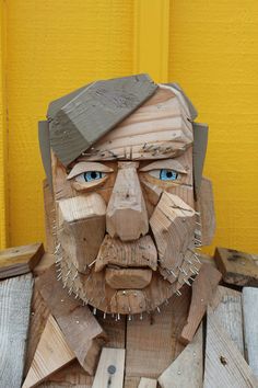 a wooden carving of a man's face with blue eyes and beard, made out of wood planks