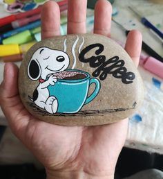 a hand holding a rock with a cartoon dog on it and coffee in the cup