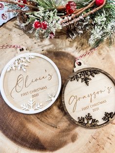 two personalized christmas ornaments sitting on top of a tree stump next to evergreen branches