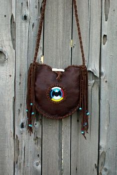 This leather tote has a beaded eagle surrounded by the four directions beadwork and measures 10 inches tall x 10 inches wide x 2 / 3/4 inches deep. This soft brown leather tote has tied fringe down the sides of the bag that are decorated with turquoise blue glass crow beads. This shoulder bag has an antler toggle for a closure. The comfortable crossbody strap measures 48 inches. If you would like to have your strap longer or shorter feel free to ask we are happy to make this change for you. This Beaded Eagle, Four Directions, Leather Craft Projects, Faux Leather Handbag, Handbag Handles, Brown Leather Totes, Pow Wow, Burberry Handbags, Hobo Handbags