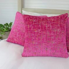 two pink pillows sitting on top of a bed next to a potted green plant