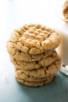 a stack of cookies next to a glass of milk on a blue counter top with a spoon