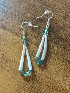 two white and green earrings sitting on top of a wooden table