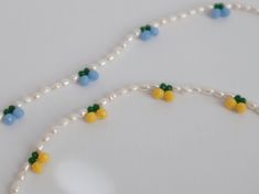 two necklaces made out of beads and pearls on a white table with blue, yellow and green beads