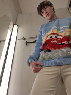 a young man is standing in front of a mirror wearing a sweater with cars on it