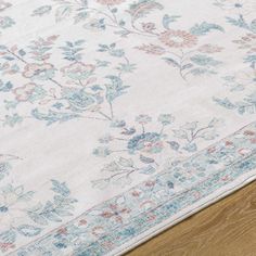 an area rug with blue and pink flowers on top of wooden flooring next to a wood table