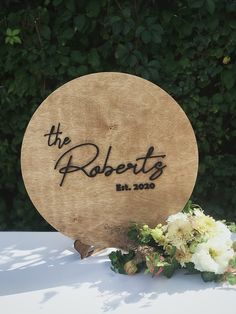 a wooden sign sitting on top of a white table next to flowers and greenery