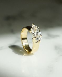 a yellow gold ring with two diamonds on it sitting on a marble countertop in front of a white background