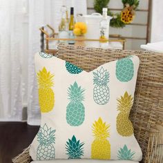 a white pillow with blue and yellow pineapples on it sitting on a wicker chair