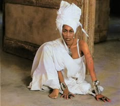 a woman in white is sitting on the ground with her hands crossed and wearing silver jewelry