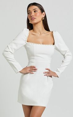 a woman wearing a white dress with long sleeves and an off the shoulder neckline