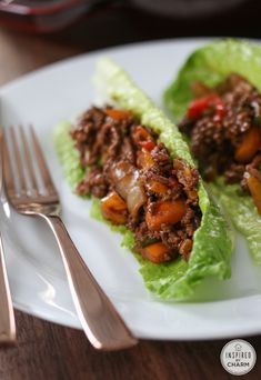 two lettuce wraps filled with meat and vegetables on a white plate next to silverware