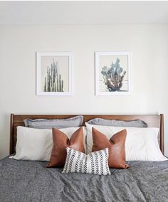 a bed with two pictures on the wall above it and some pillows in front of it