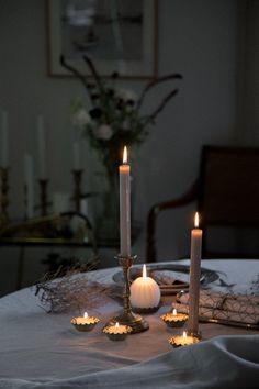 candles are lit on a table with white linens and other decorations in the background