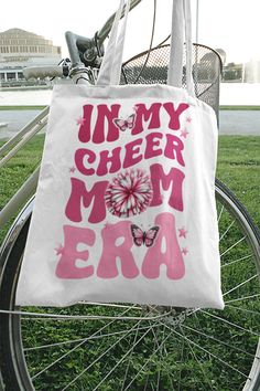 a white bag that says, i am my cheer mom era on it sitting next to a bicycle