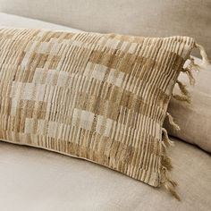 a close up of a pillow on a couch with a tan background and fringed edges