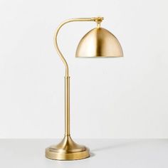 a gold desk lamp on a white surface with a cord plugged into the base