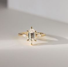 a gold ring with an emerald cut diamond in the center and three small diamonds on each side