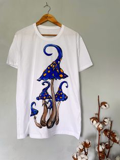 Discover the charm of nature with our exclusive hand-painted mushroom t-shirt. Each piece is meticulously hand-painted, ensuring 100% uniqueness. The minimalist design effortlessly complements any outfit in your wardrobe. ✨Customize the color scheme to suit your style. ✨Modify the shape and number of mushrooms to create your perfect look. ✨The color combinations for the mushrooms are limitless, allowing for a truly personalized touch. The drawing is applied by hand with brushes and special paints. Therefore, each product is not 100% similar to the previous one and is unique. Made from high-quality cotton material, our mushroom t-shirt offers unbeatable comfort and breathability, ensuring you feel great all day long. Whether you're out on the town or lounging at home, this t-shirt is the pe Hand Painted White T-shirt For Summer, White Cotton T-shirt With Mushroom Design, Artistic Hand Painted Short Sleeve T-shirt, White Cotton Tops With Mushroom Print, Hand Painted Cotton Graphic Tee, Hand Painted Short Sleeve Graphic Tee, Hand Painted Short Sleeve Cotton Top, White Short Sleeve T-shirt With Mushroom Design, Artistic Hand Painted Crew Neck Top