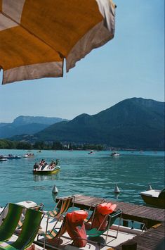 chairs and umbrellas are sitting on the dock by the water with boats in the distance