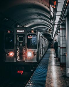 a subway train pulling into the station with its lights on and people standing next to it