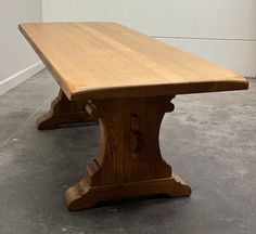 a large wooden table sitting on top of a cement floor next to a white wall