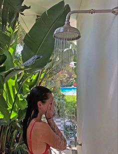 a woman in a red bathing suit standing under a shower head and spraying her hair