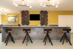 a kitchen with three bar stools and two paintings on the wall behind it,