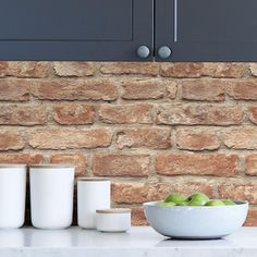 a bowl of green apples sitting on top of a counter next to cups and bowls